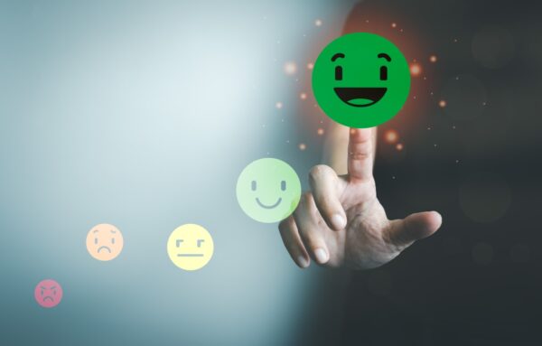 Afbeelding van een hand die een groene, lachende emoji aanraakt, omringd door andere emoji's die verschillende emoties uitdrukken, variërend van boosheid tot blijdschap.
